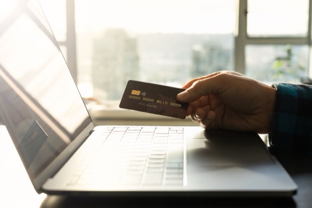 Photograph: hand holding a card in front of a laptop