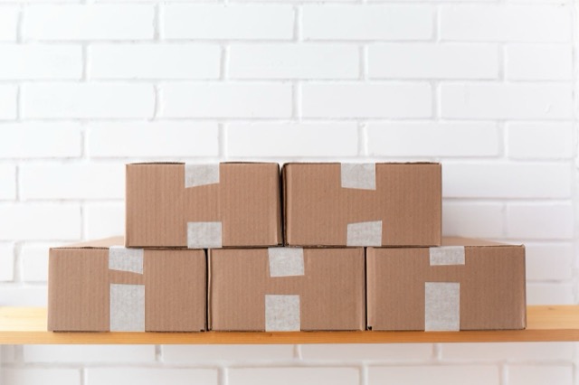 Photograph: taped brown boxes on a shelf against white brick